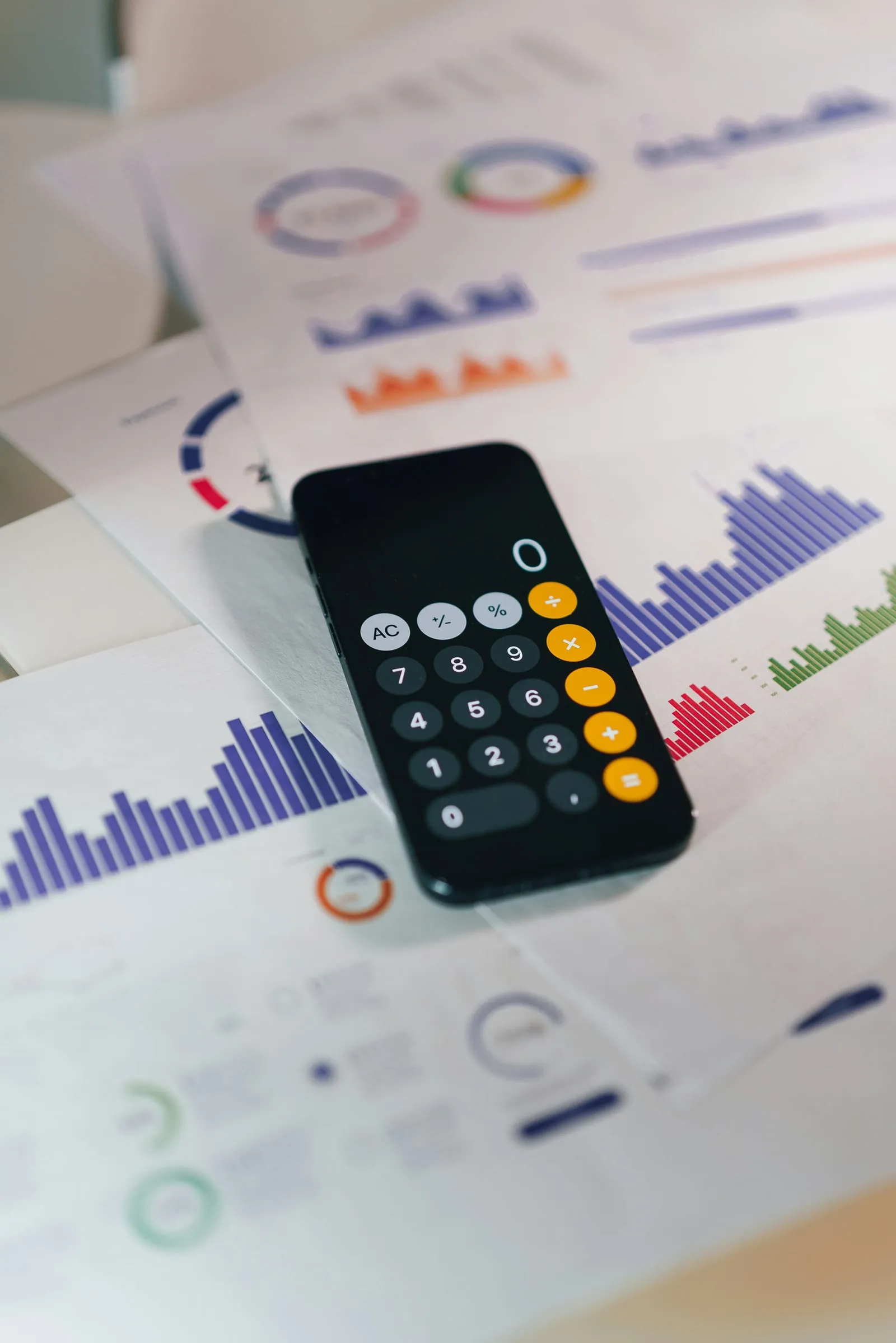 Phone showing a calculator app rests on printed pages covered in colorful bar charts and donut graphs