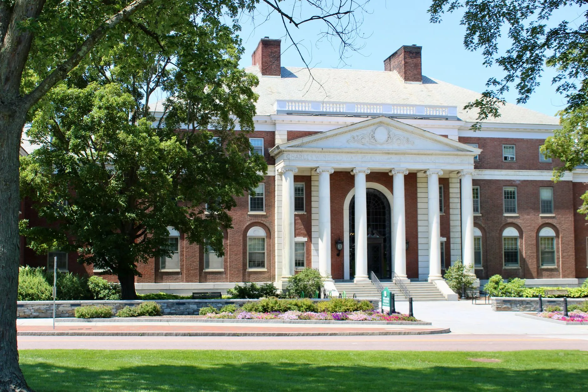 Red brick academic building with white Ionic columns, stone steps and a landscaped lawn on the University of Vermont campus in Burlington.