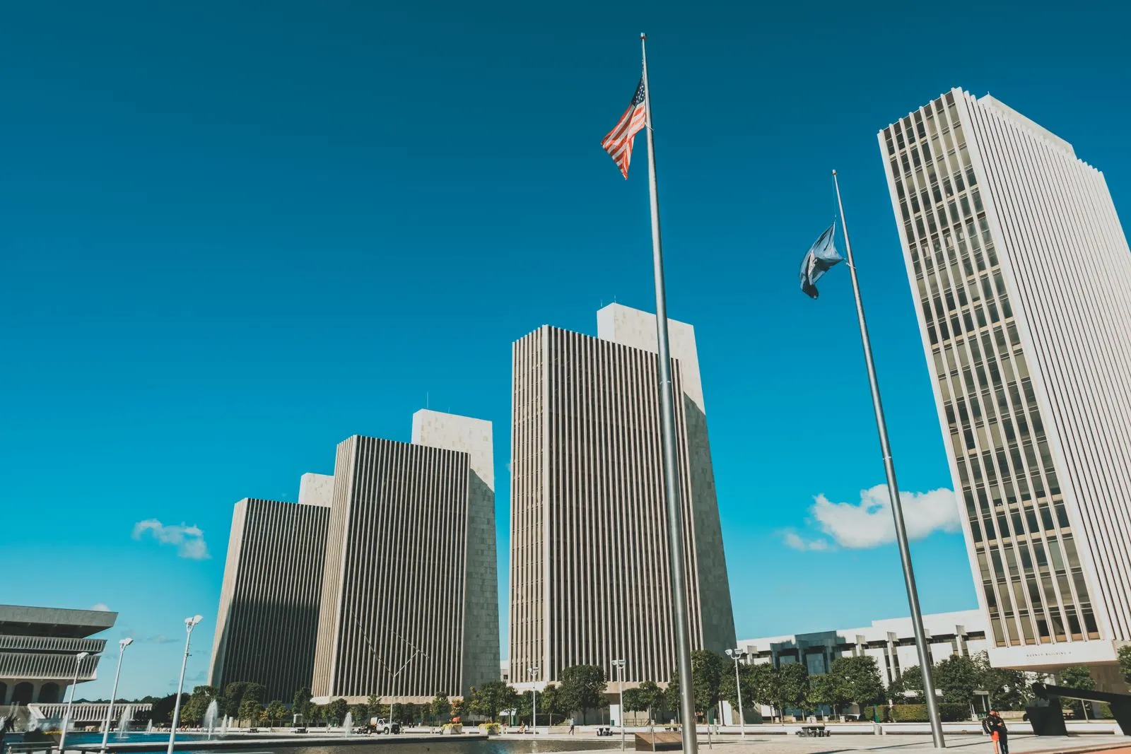 Tall modern office towers around a wide plaza with flagpoles under a deep blue sky