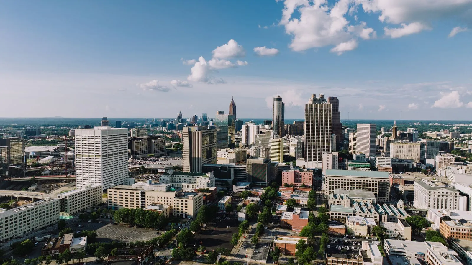 A downtown skyline seen from above, office towers rising out of green trees and lower blocks