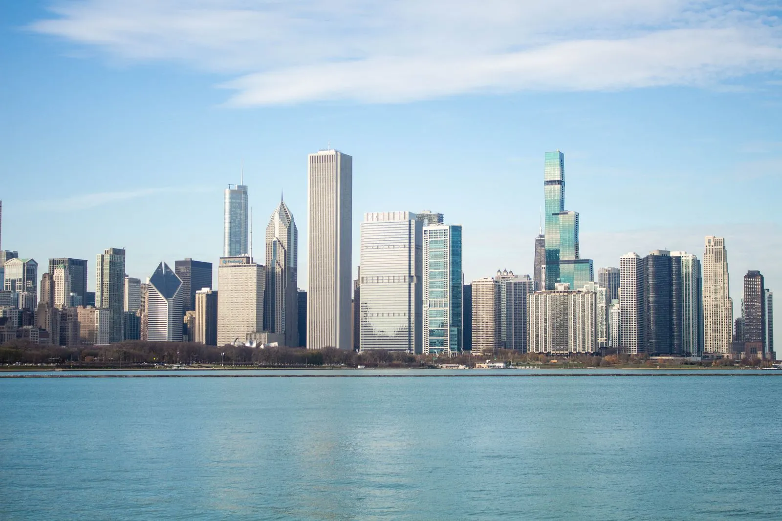 A long skyline of towers along the shore of a calm, wide lake under a pale sky