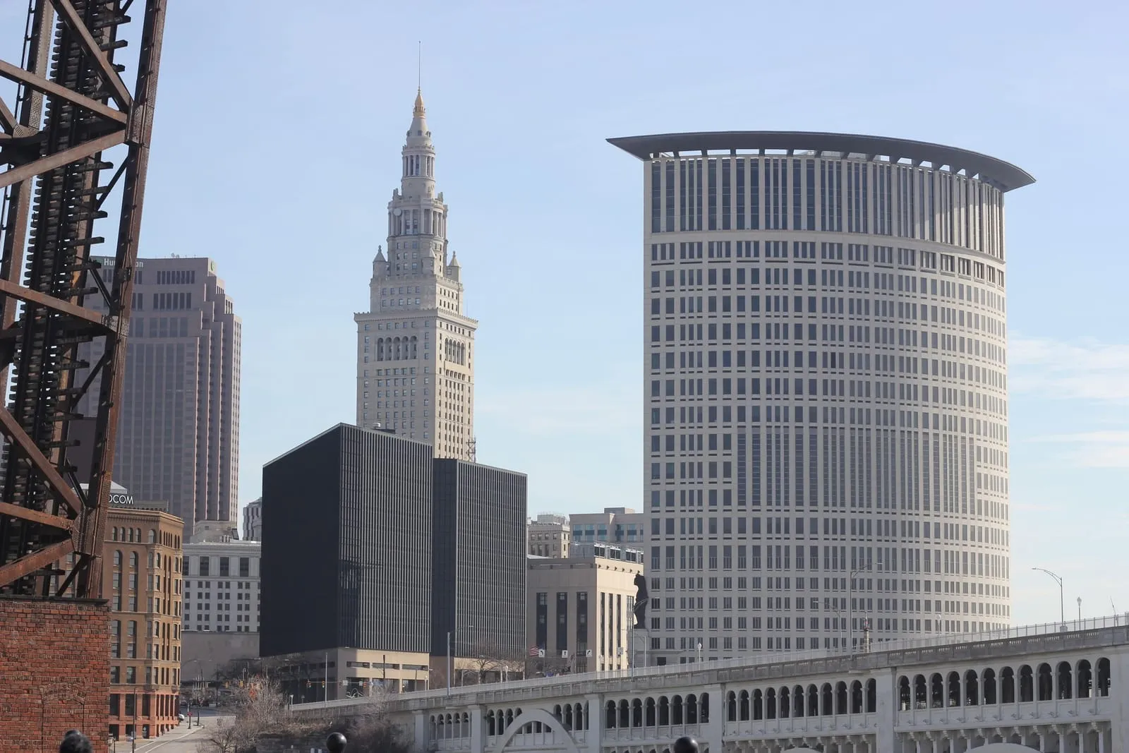 A tall stepped stone tower beside a round modern high-rise, seen from a bridge