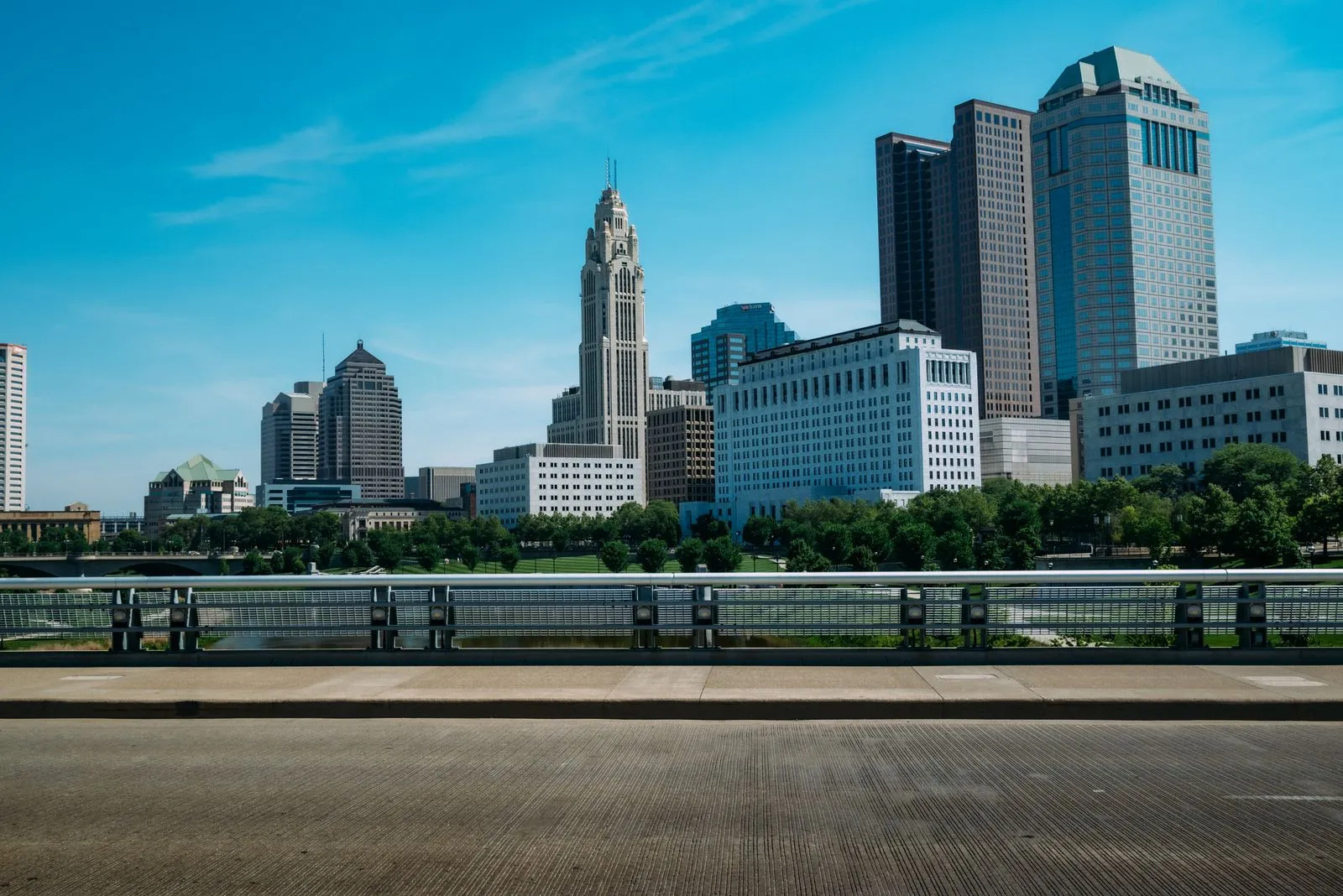 Downtown high-rises against a bright blue sky with scattered clouds, street trees below