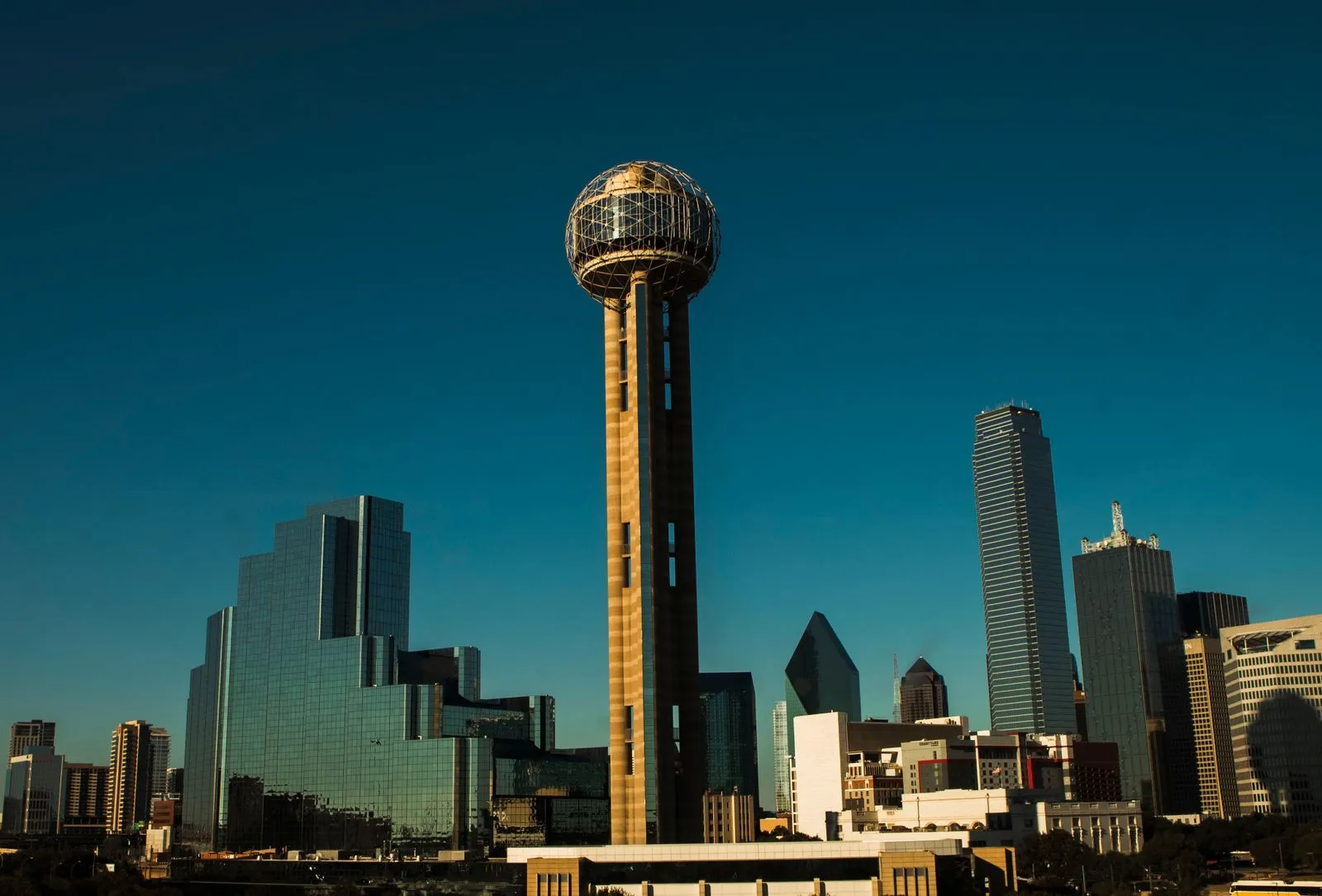 A tower topped by a lattice ball among glass skyscrapers against a deep blue sky