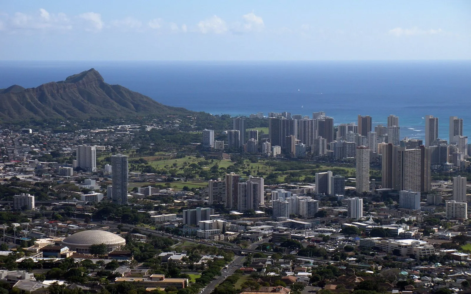 Aerial view of high-rise towers along a shoreline with a broad volcanic crater behind them and the ocean beyond