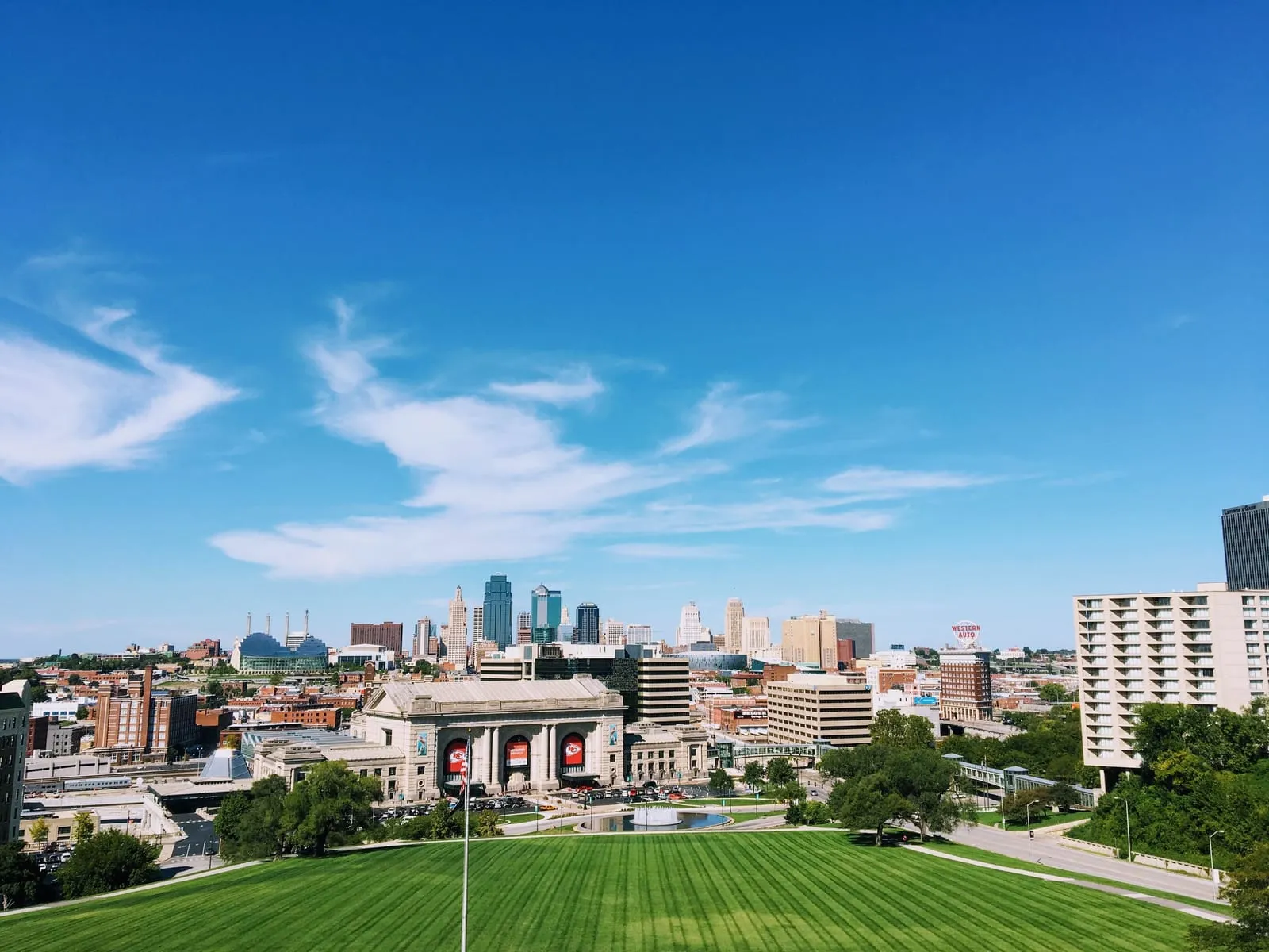 A grand stone train station and lawn in front of a downtown skyline under a blue sky