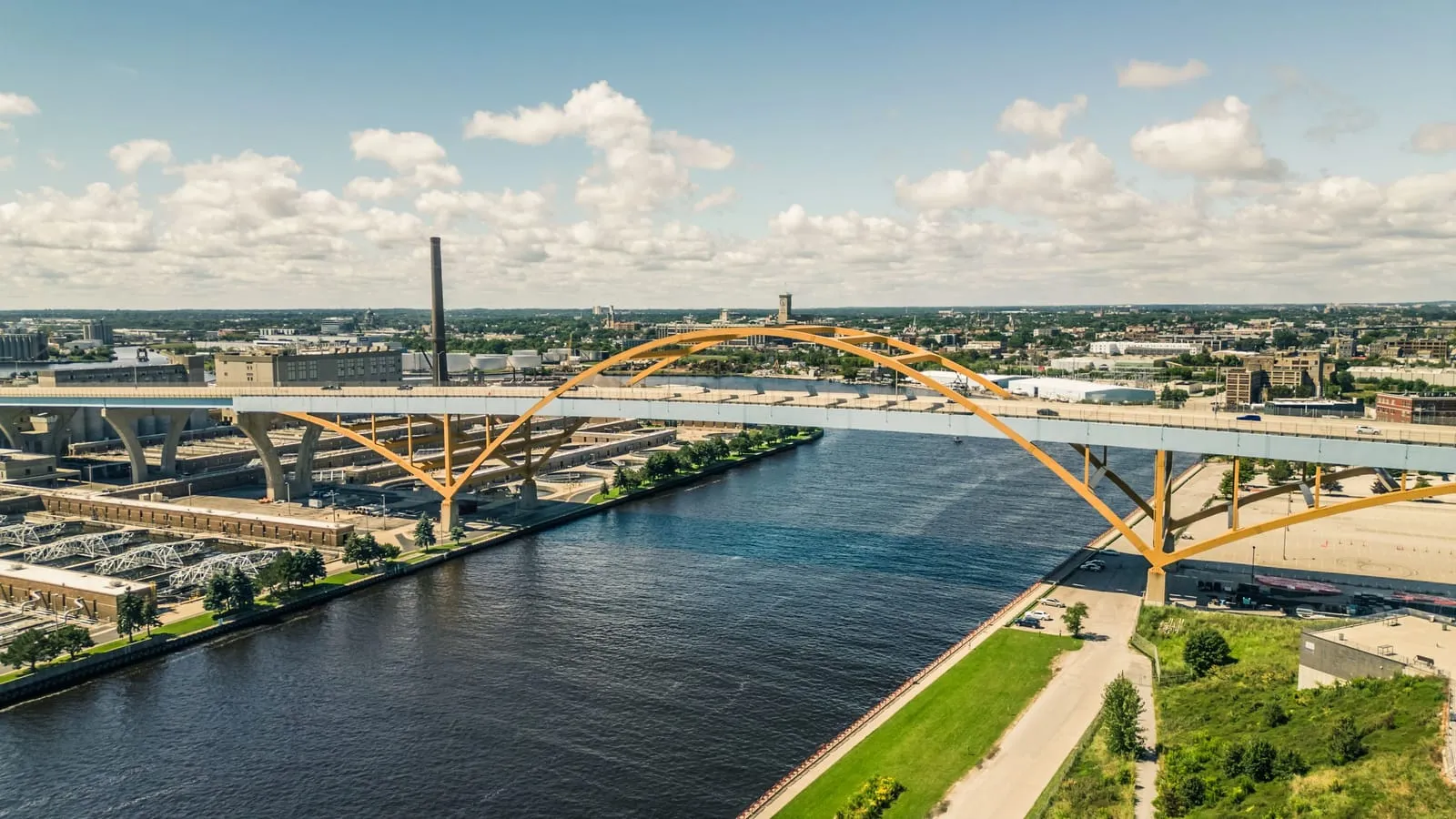 A yellow steel arch bridge carrying a highway across a river into a city, seen from above