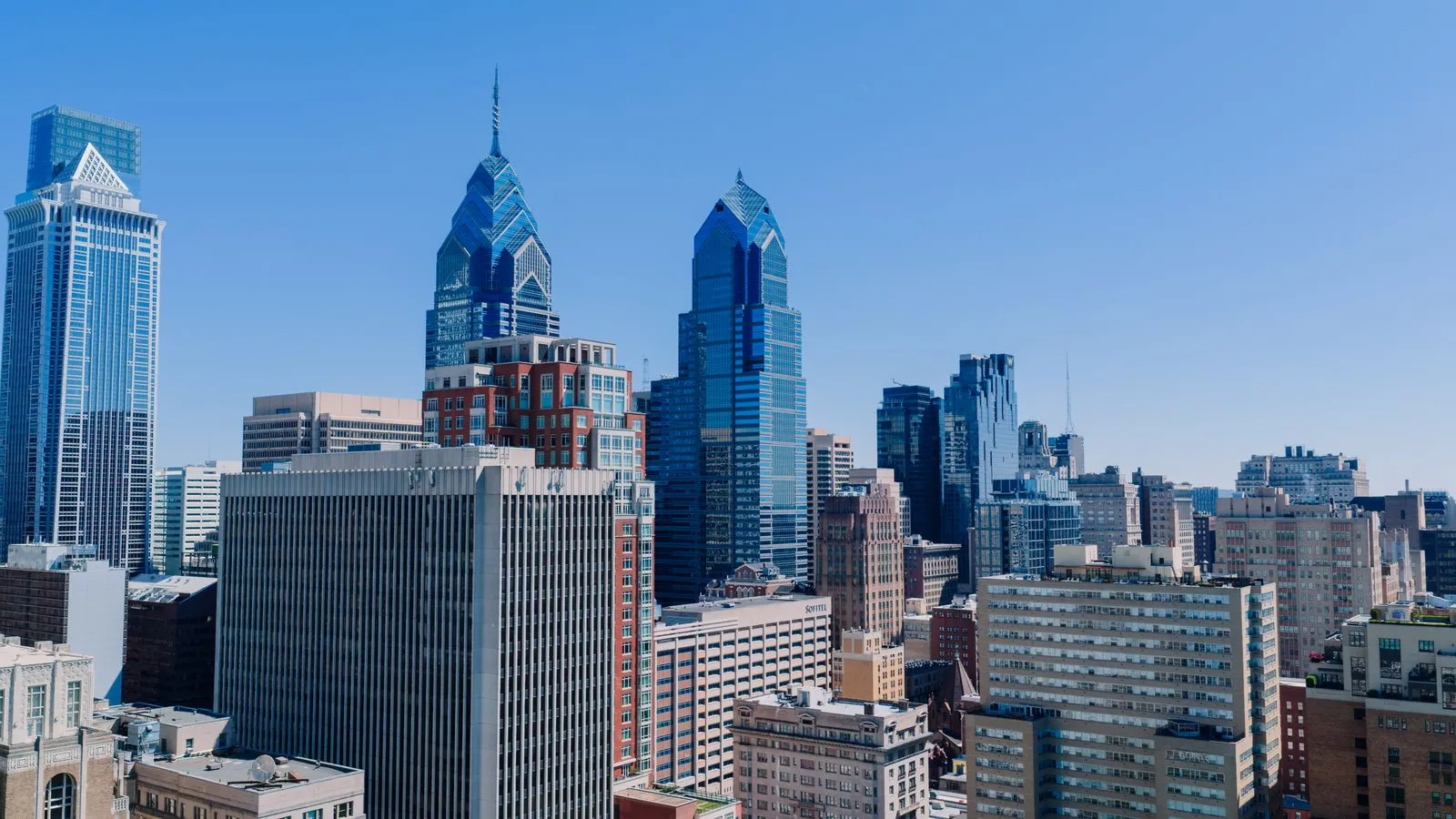 Two blue glass towers with pointed crowns above a dense downtown under a clear sky
