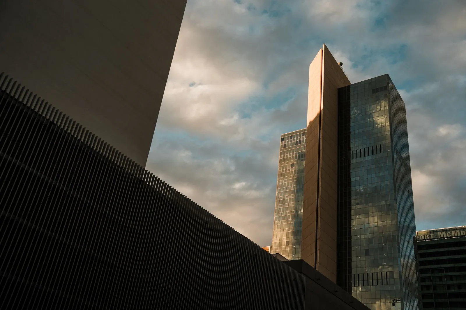 Two glass towers catching the light of a cloudy sunset, the dark edge of another building in the foreground