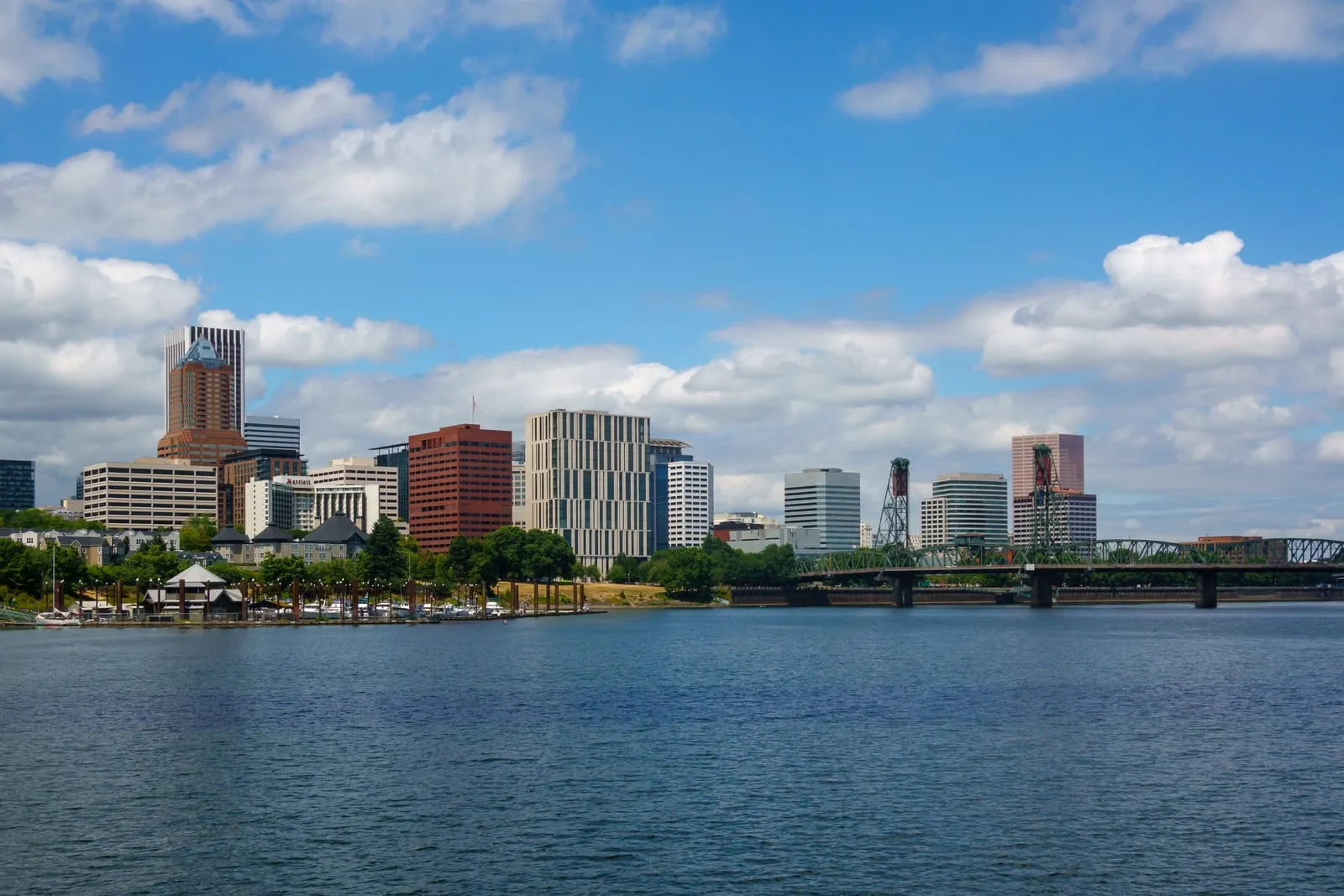 A riverfront of mid-rise buildings and a steel lift bridge under white clouds and blue sky