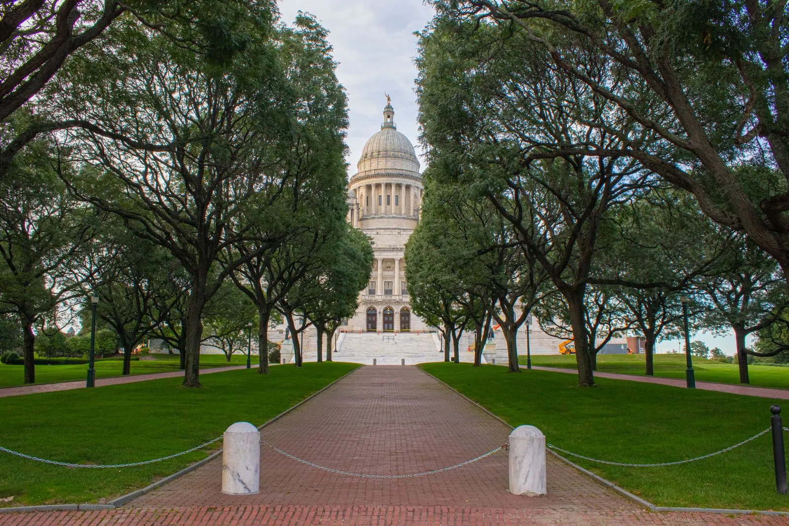 A brick path between rows of trees leading to a white domed capitol building