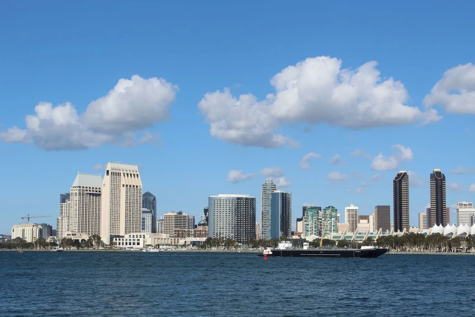 A bayfront skyline of towers across blue water under scattered white clouds