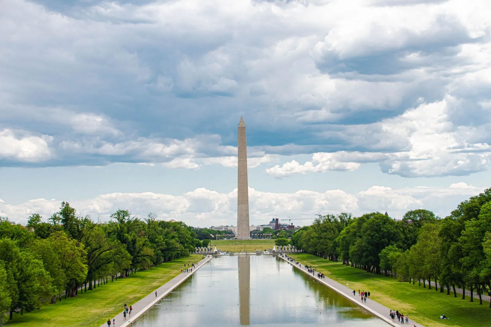 A white stone obelisk at the far end of a long reflecting pool lined with trees