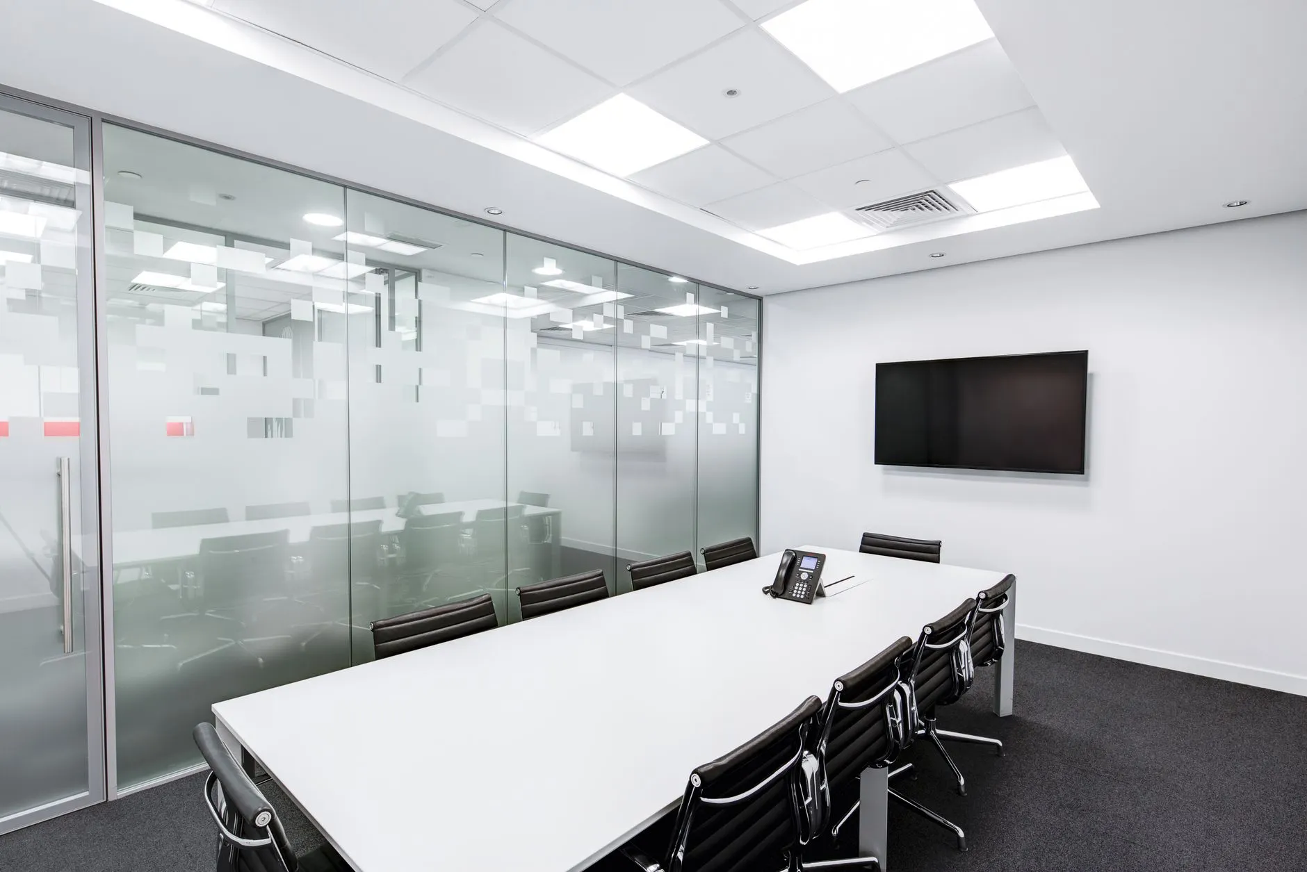 An empty glass-walled boardroom with a long conference table and rows of office chairs