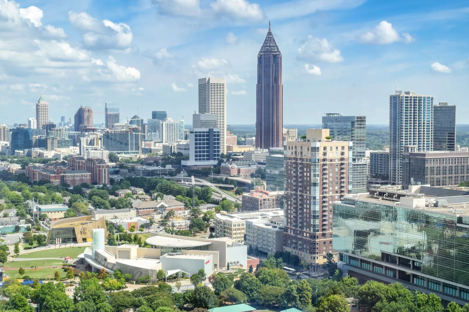A downtown skyline with a tall spired tower, seen from above over green parkland and low buildings