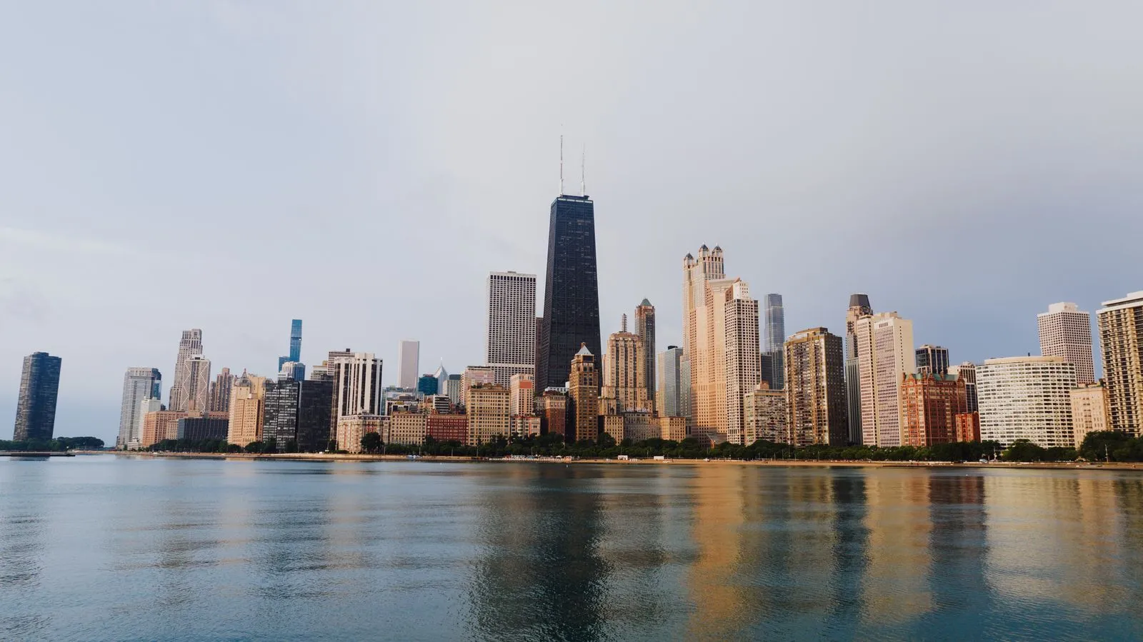 A lakefront skyline led by a tall dark tower with twin antennas, reflected in calm water