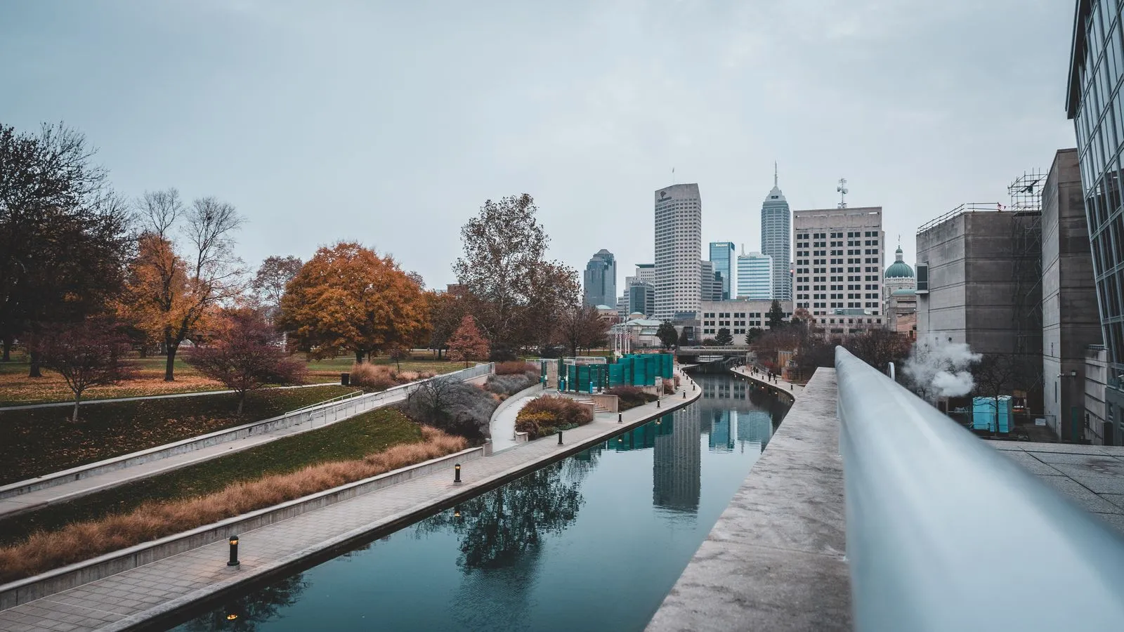 An urban canal walk lined with autumn trees, downtown towers ahead