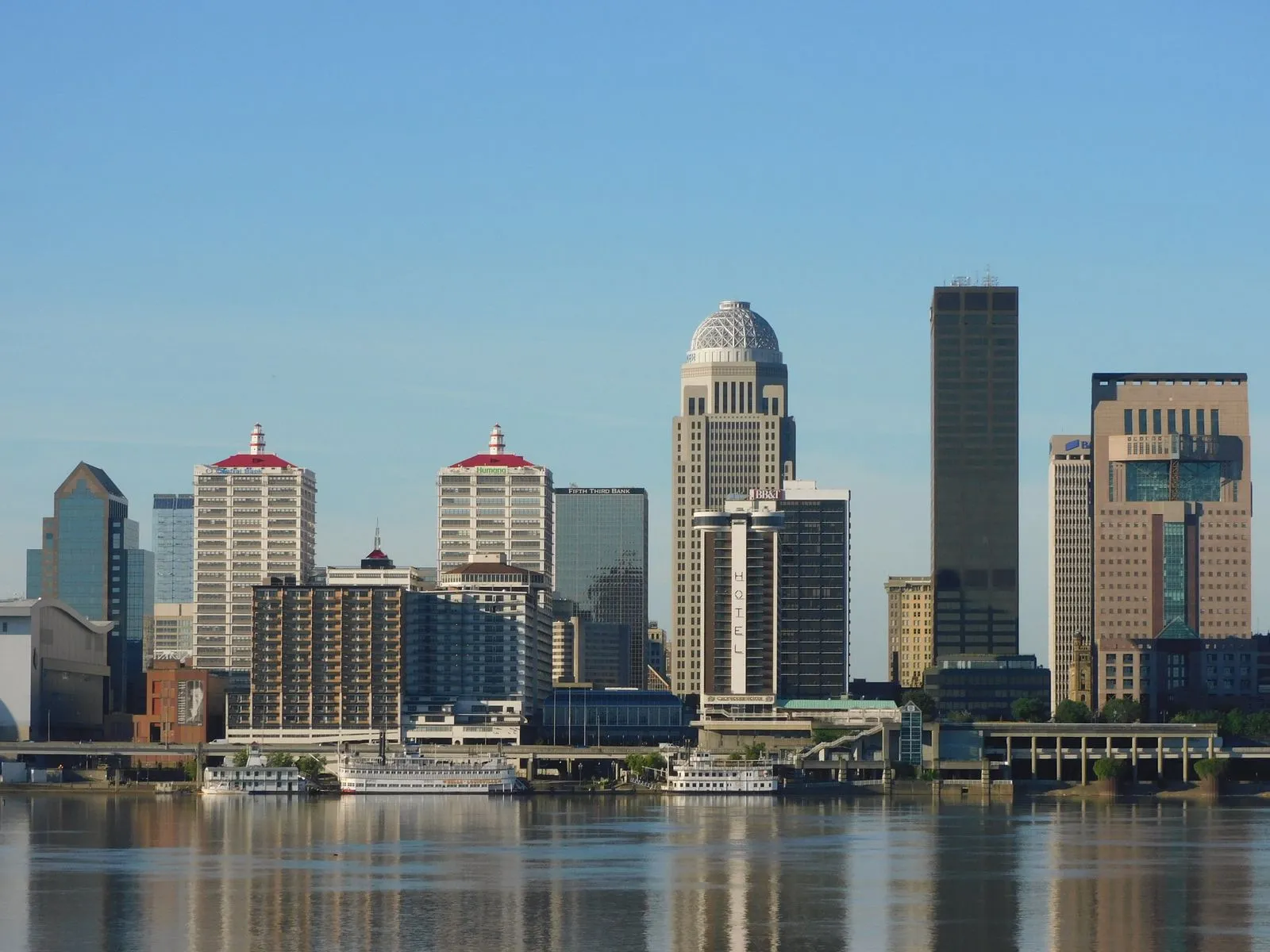 A riverfront skyline of office towers reflected in a wide river