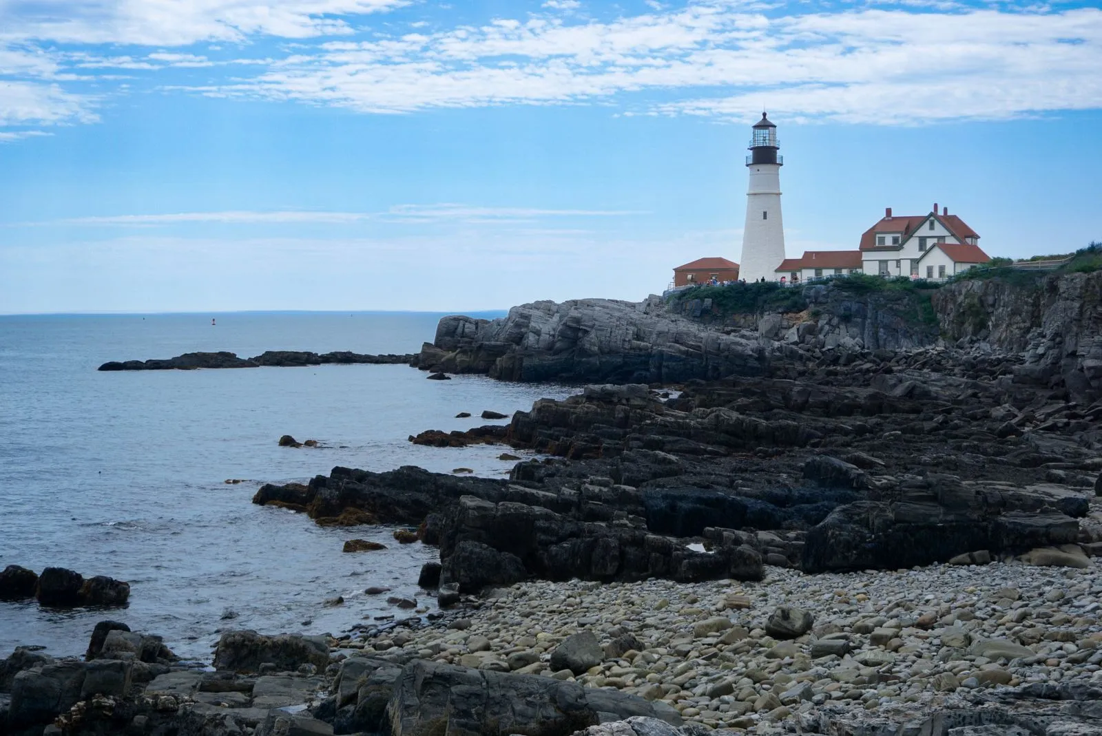 A white lighthouse and red-roofed keeper's house on a rocky point above the sea