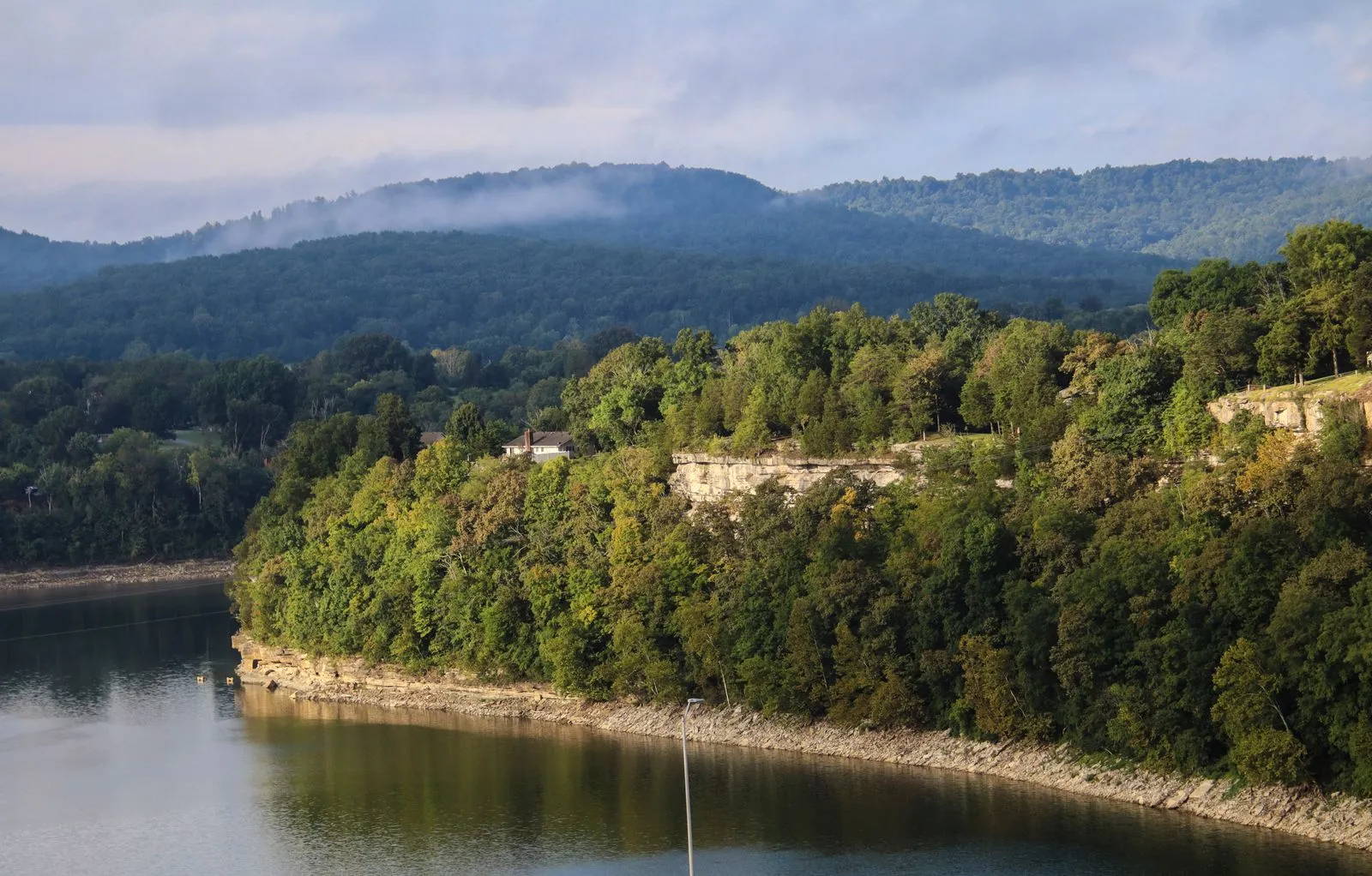 A wooded limestone bluff along a calm lake, forested hills fading behind