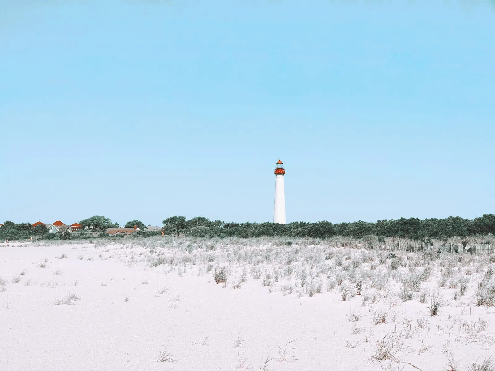 A white lighthouse beyond pale dunes and beach grass under a clear sky
