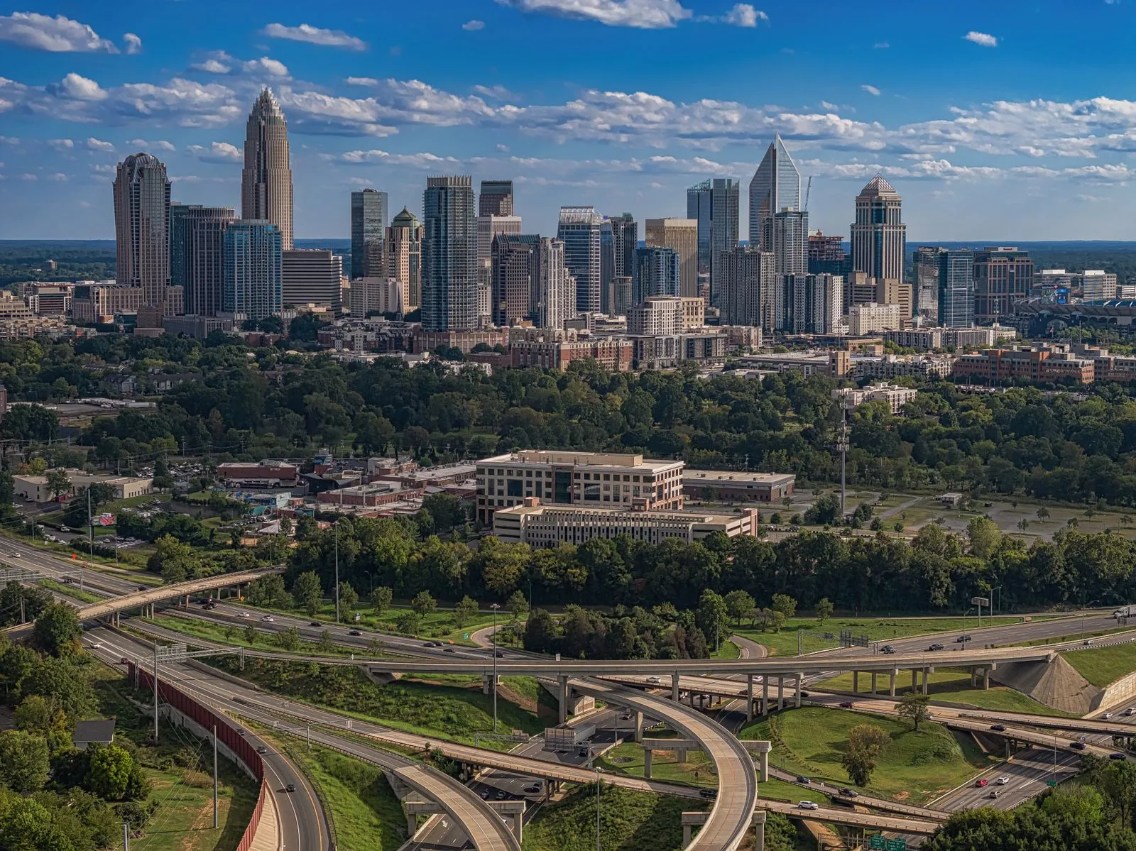 A downtown skyline rising above green trees, a looping highway interchange in front