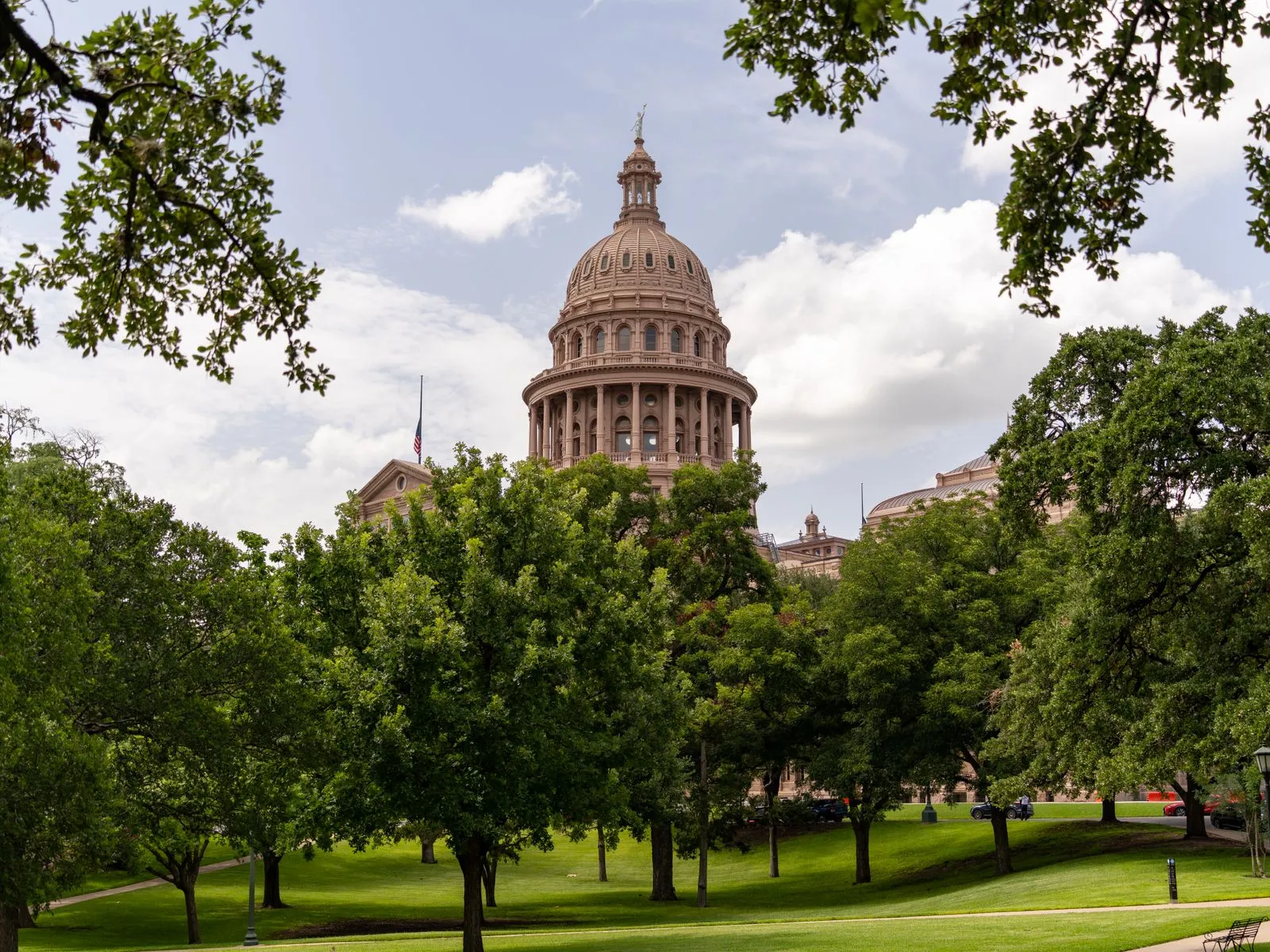 A domed government building of pale stone seen across a lawn framed by oak trees
