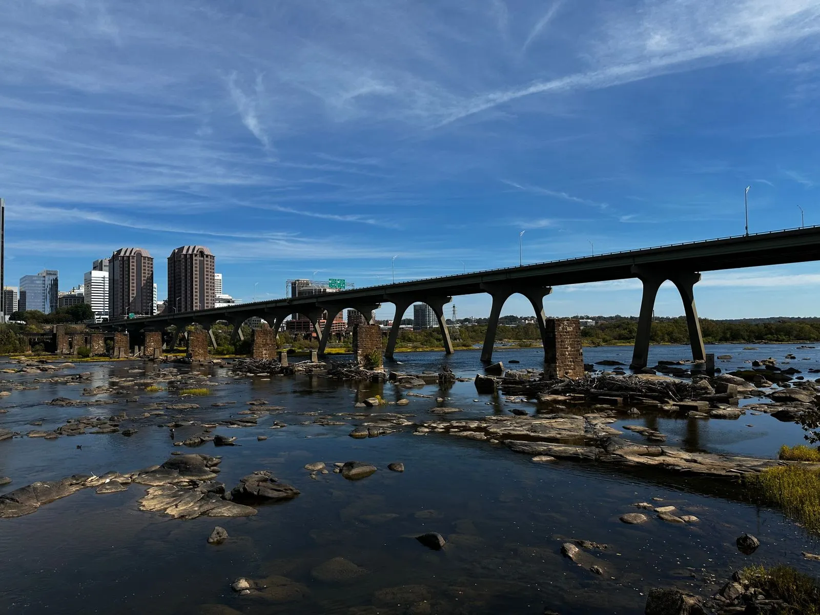 A concrete arched bridge crossing a rocky river toward a few city towers